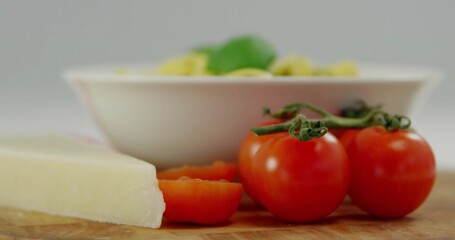 Cluster and halved tomatoes resting atop cutting board in kitchen, with cheese wedge, pasta bowl