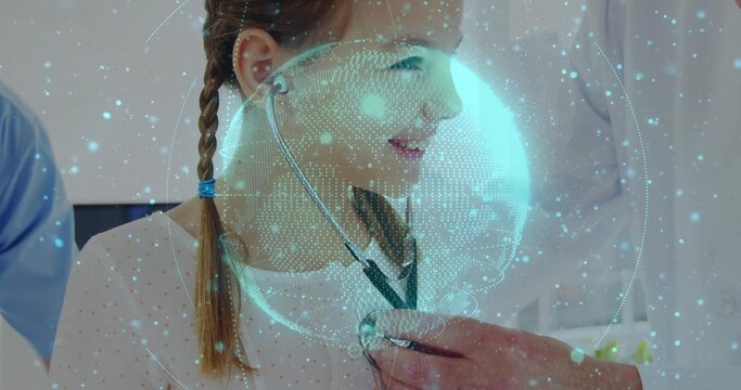 Lab coat doctor placing stethoscope on girl in clinic, with blue scrubs staff and hologram globe