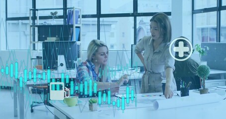 Business casual women analyzing printed charts at office desk, with laptop, pen and coffee