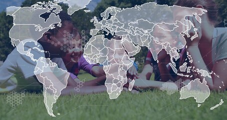 Lying diverse children studying tablet computer on lush green lawn in park, with world map overlay