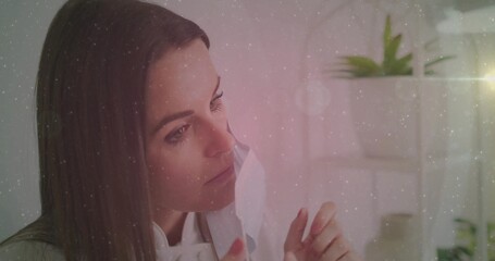 Woman in light blouse applying sheet mask in home vanity, with white shelf and green plants