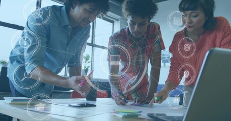 Collaborating three colleagues leaning over papers on table in office, with markers and overlay