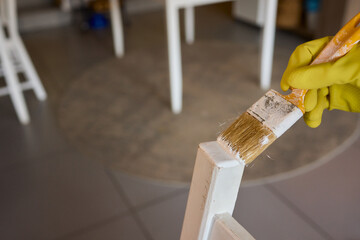 Engage in DIY chair restoration using a paint brush and protective gloves for the process