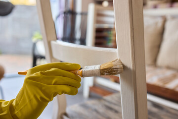 Engage in DIY chair restoration using a paint brush and protective gloves for the process