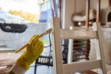 Engage in DIY chair restoration using a paint brush and protective gloves for the process