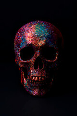 A glitter covered pink purple blue skull shines in vivid multicolored reflections against a dark background. The sparkling surface creates a stylish, mysterious, and artistic decorative object