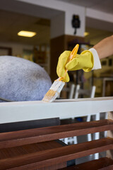 Engage in DIY chair restoration using a paint brush and protective gloves for the process