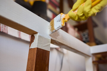 Engage in DIY chair restoration using a paint brush and protective gloves for the process