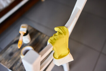 Engage in DIY chair restoration using a paint brush and protective gloves for the process