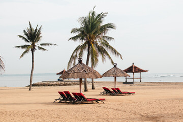 Red beach loungers under tropical umbrellas on sandy shore