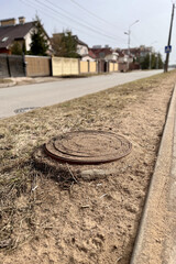 A rusty iron hatch covered grains of sand and the ground with a pattern above an observation well