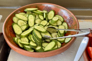 A bowl of fresh cucumber slices a versatile and healthy ingredient in various cuisines, displayed with tongs, ready to be enjoyed as a side dish or used in recipes