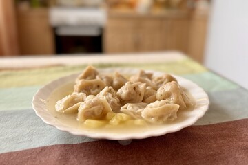 Soup with beef dumplings and potatoes in a white plate on a multi colored tablecloth on a table at home