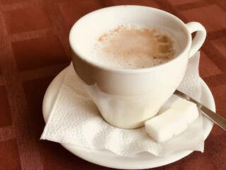 A coffee cup within pieces of white sugar placed on a saucer, resting on a red table