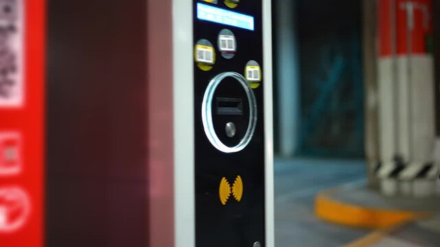 Close up of a hand inserting a parking ticket into the exit machine to lift the barrier gate. Transportation, parking system, payment process, urban service, automation, and modern city convenience