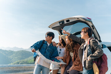 Happy Young Asian man and woman friends road trip travel countryside on summer holiday vacation. Generation z people enjoy outdoor active lifestyle sit on EV car trunk and looking direction on a map.