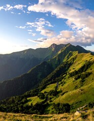 Lush green mountain slopes meet a vibrant blue sky filled with fluffy white clouds at sunset, showcasing a picturesque landscape.