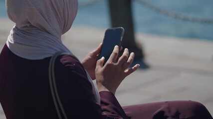 Woman using smartphone by the water in a sunny location - Powered by Adobe