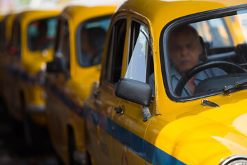 A row of vintage yellow taxis in Kolkata, India, lined up with drivers waiting inside—an iconic symbol of the city’s timeless charm and bustling street culture.