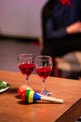 A colorful Halloween party moment with red wine glasses, fresh salad, and a vibrant maracas toy on a wooden table, symbolizing festive joy, music, and the spirit of creative celebration.