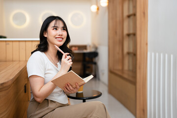 Dreaming woman looking away while resting at cafe and writing , young woman enjoying free time and planning to do list in notebook.