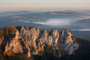 Majestic mountain range during sunrise, golden light on rocky cliffs, mist in valleys, dramatic natural background.
