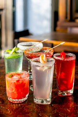 Vibrant assortment of colorful cocktails on a rustic wooden bar table, perfect for a happy hour party or summer celebration menu.