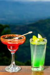 Two colorful cocktails to enjoy happy hour at the bar, with a breathtaking view of the mountains at sunset in a vacation resort.
