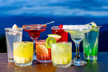 Row of colorful tropical cocktails on a terrace bar with a stunning mountain view at sunset, embodying a luxury vacation and travel getaway.