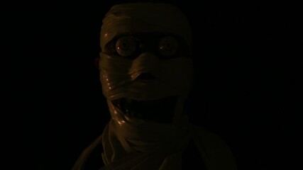 Portrait of man in creepy mummy wrapped custom with bandages wearing his mask and moving his face to look funny and creepy, dark lighting.