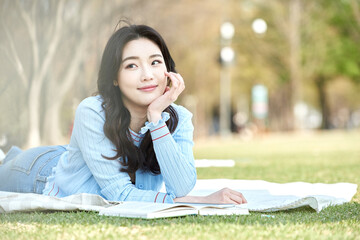Young female reading book outdoors on spring picnic blanket in park