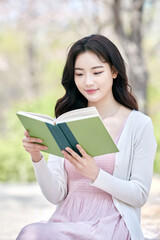 Young Asian female reading a book outdoors in spring park, relaxing and learning