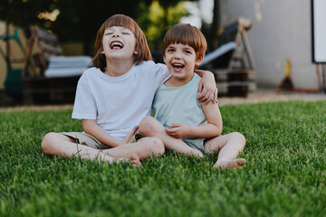 Fototapeta premium Two happy boys laughing together outdoors, enjoying a sunny day on the grass. Their carefree spirit and joy shine through in this vibrant moment.