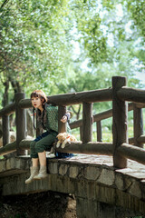 Fototapeta premium Girl sitting on a bridge holding a stuffed toy in a sunny park.