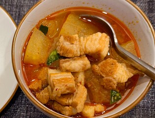 Southern Thai red curry with pork belly and winter melon, spicy soup with aromatic herbs; authentic Thai cuisine, close-up background with copy space