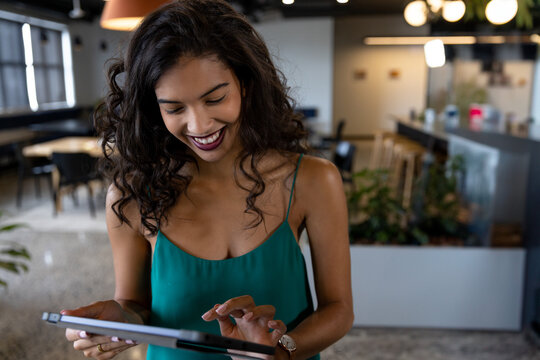 Young African American woman using tablet in modern office lounge, wearing smartwatch and smiling