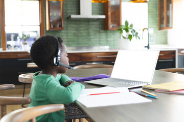 Open laptop displaying blank screen resting on dining table near green backsplash and pencils