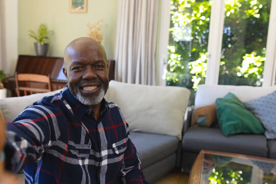 Senior African American man taking selfie with smartphone on sofa in living room, copy space