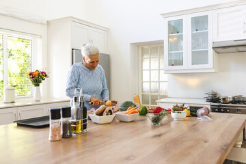 Senior woman chopping vegetables on wooden island in home kitchen, with board, knife, copy space
