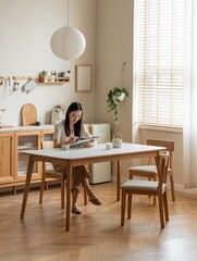 A woman reading a magazine at a wooden dining table in a minimalist kitchen.
