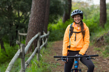 White woman smiling on mountain bike trail beside fence, wearing helmet, copy space