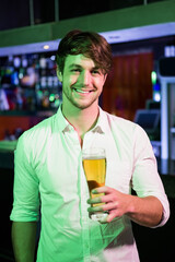 Man holding pint glass at pub counter under green lights, showing liquor bottles and POS terminal