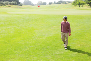 Naklejka premium Golfer walking across vibrant green fairway toward red flag, holding putter with red glove