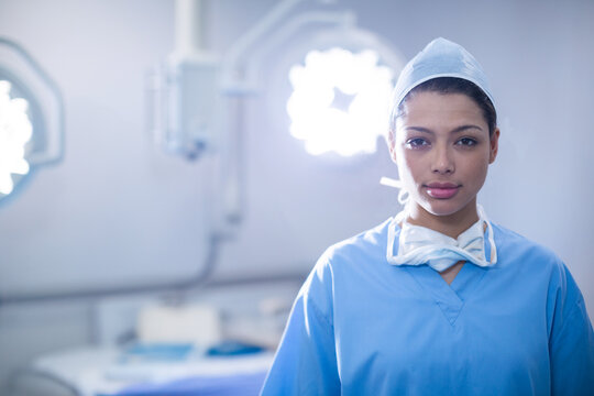 African American woman surgeon standing in operating room with surgical lights and mask, copy space - Powered by Adobe