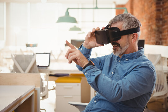 Man wearing VR headset pointing at interface on desk with laptop and green lamps