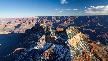 Aerial view of a vast, colorful canyon under a bright blue sky, with snow dusting some of the formations