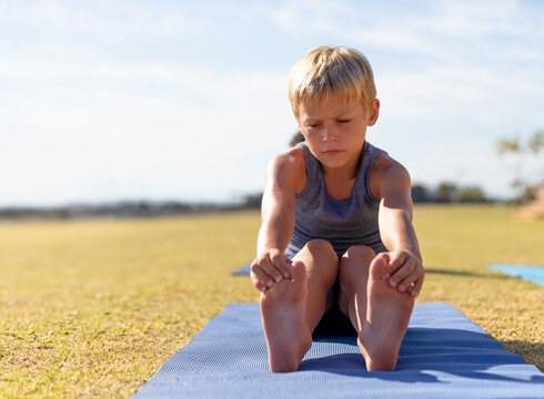 Fototapeta Young boy practicing yoga on mat outdoors, concentrating on stretching exercise, copy space