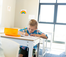 In school, young boy concentrating on writing at desk in bright classroom, copy space
