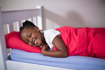 Smiling child lying in bed with red blanket, enjoying cozy morning at home