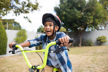 Naklejka premium Excited boy riding bicycle in backyard, wearing helmet and enjoying outdoor fun, copy space